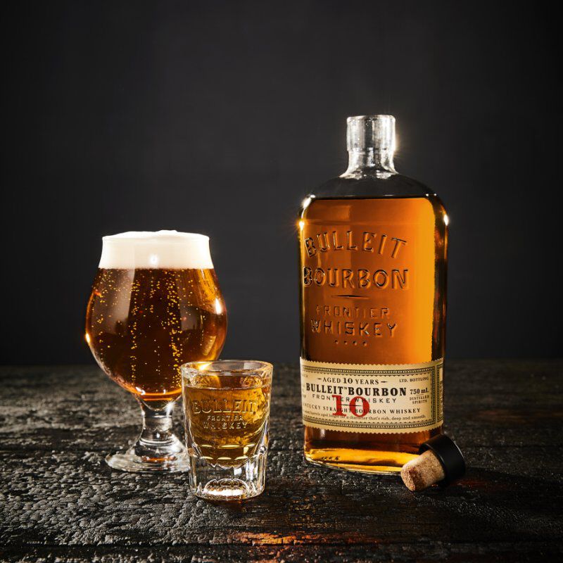 Bulleit Bourbon 10 Year Old, tulip glass, shot glass on a charred wood surface