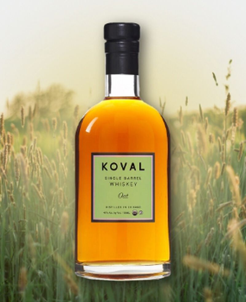 Bottle of KOVAL Oat Whiskey in front of oat field