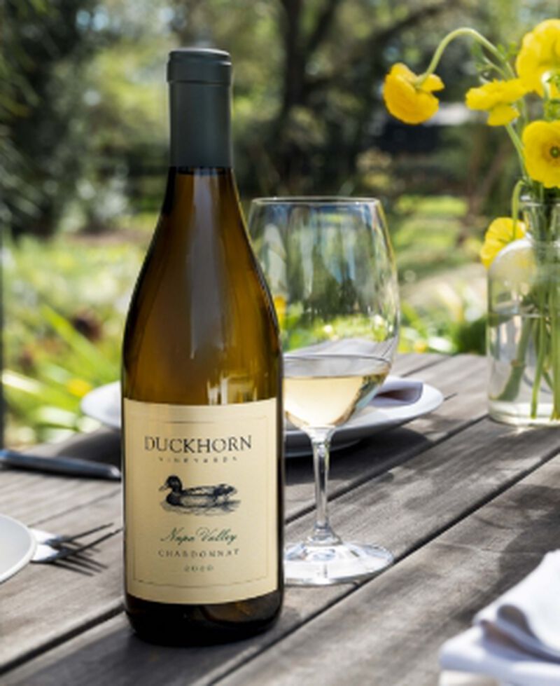 A bottle of Duckhorn Vineyards Napa Valley Chardonnay with a glass on an outdoor table