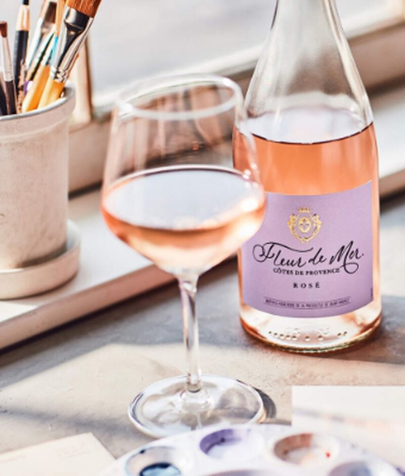 A bottle of Fleur de Mer Cotes De Provence French Rosé Wine with a glass and paint supplies