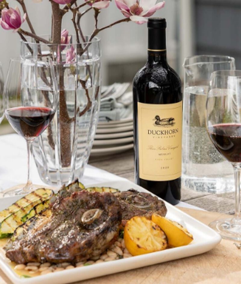 Bottle of Duckhorn Vineyards "Three Palms Vineyard" Merlot Calistoga 2019 with a grilled steak and vegetables dinner and wine glasses