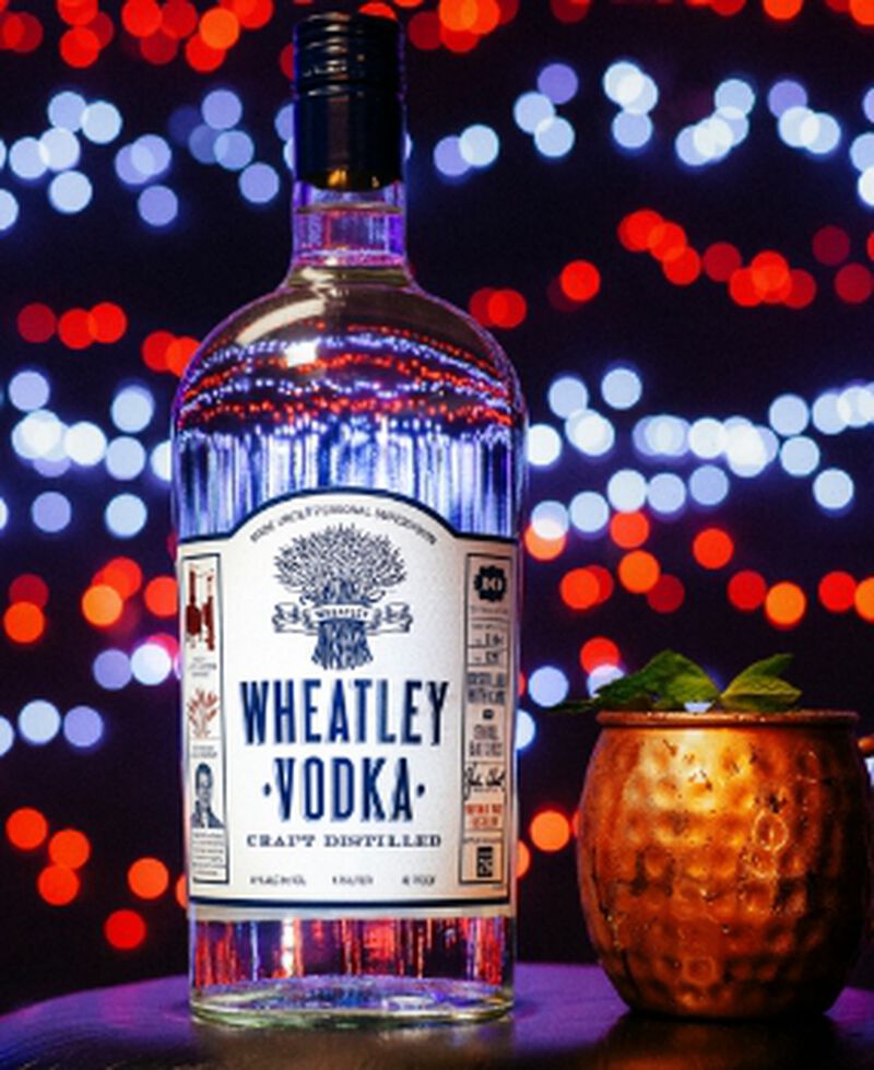A bottle of Wheatley Vodka with a copper mug in front of lights