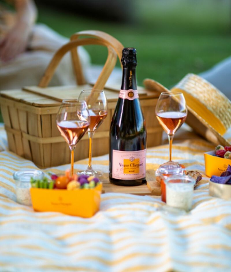 Bottle of Veuve Clicquot Rosé on a blanket with a picnic basket, glasses, and snacks