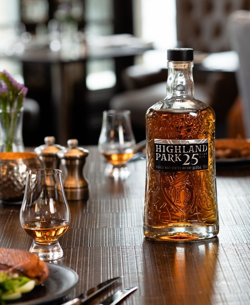 A bottle of Highland Park 25 Year Old Single Malt Whiskey on a table with dinner and glasses