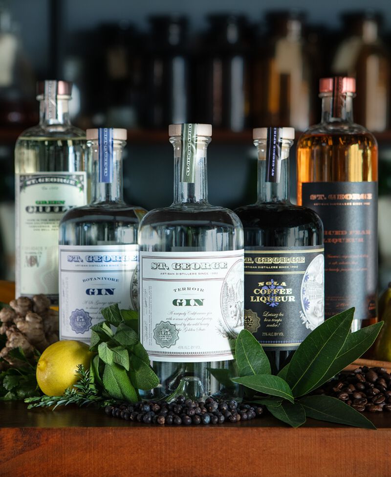 A group of St. George Spirits bottles sitting on a bar with greenery and a lemon
