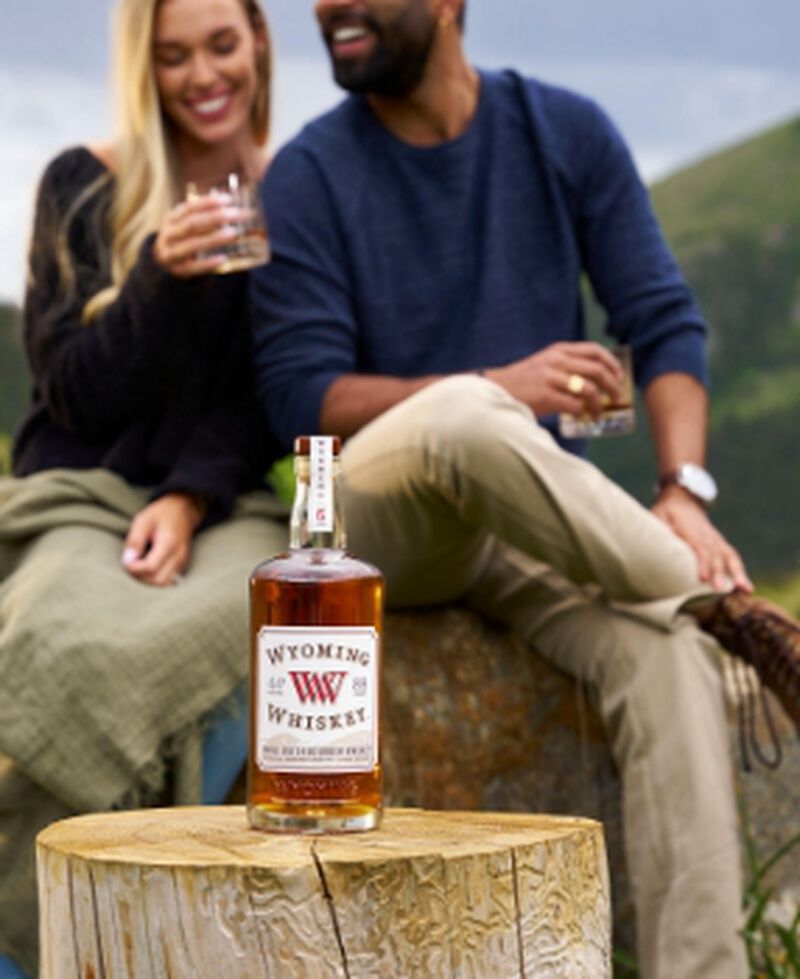 A bottle of Wyoming Whiskey Small Batch Bourbon Whiskey with two people enjoying glasses of it