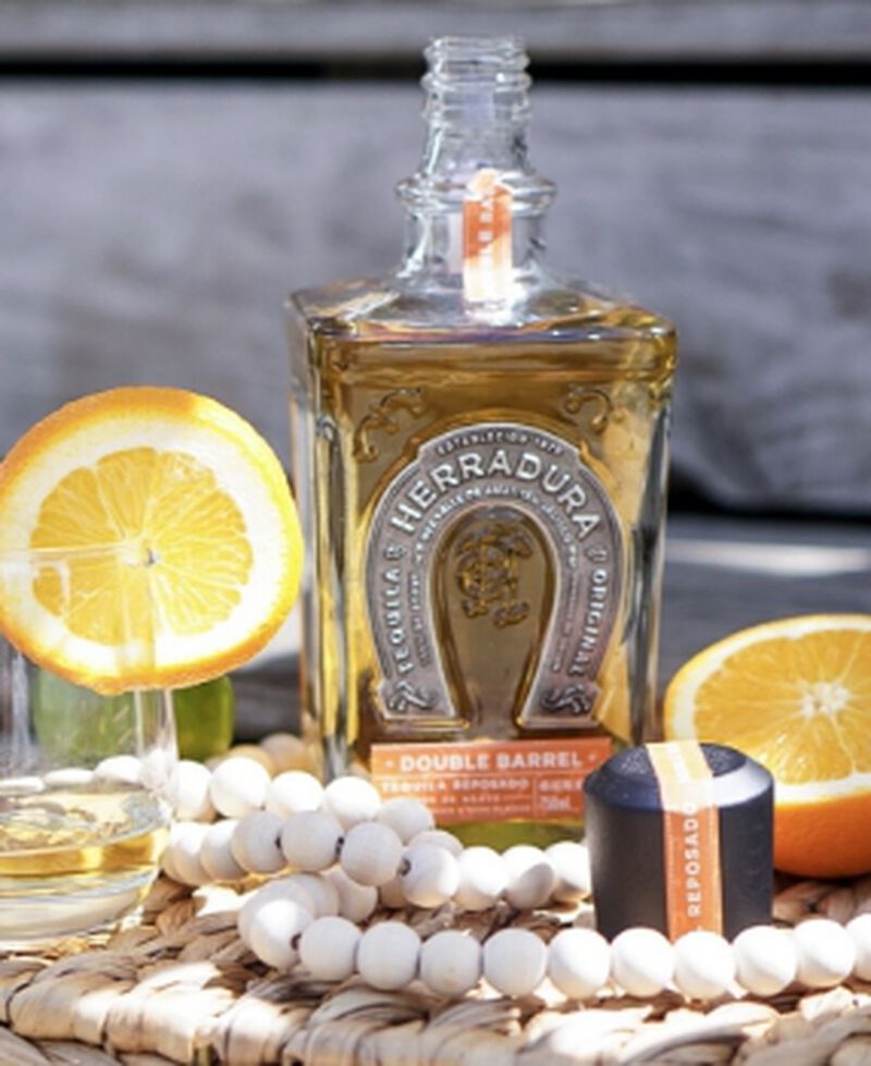 A bottle of Tequila Herradura Double Barrel Reposado S1B58 with glasses and citrus outside