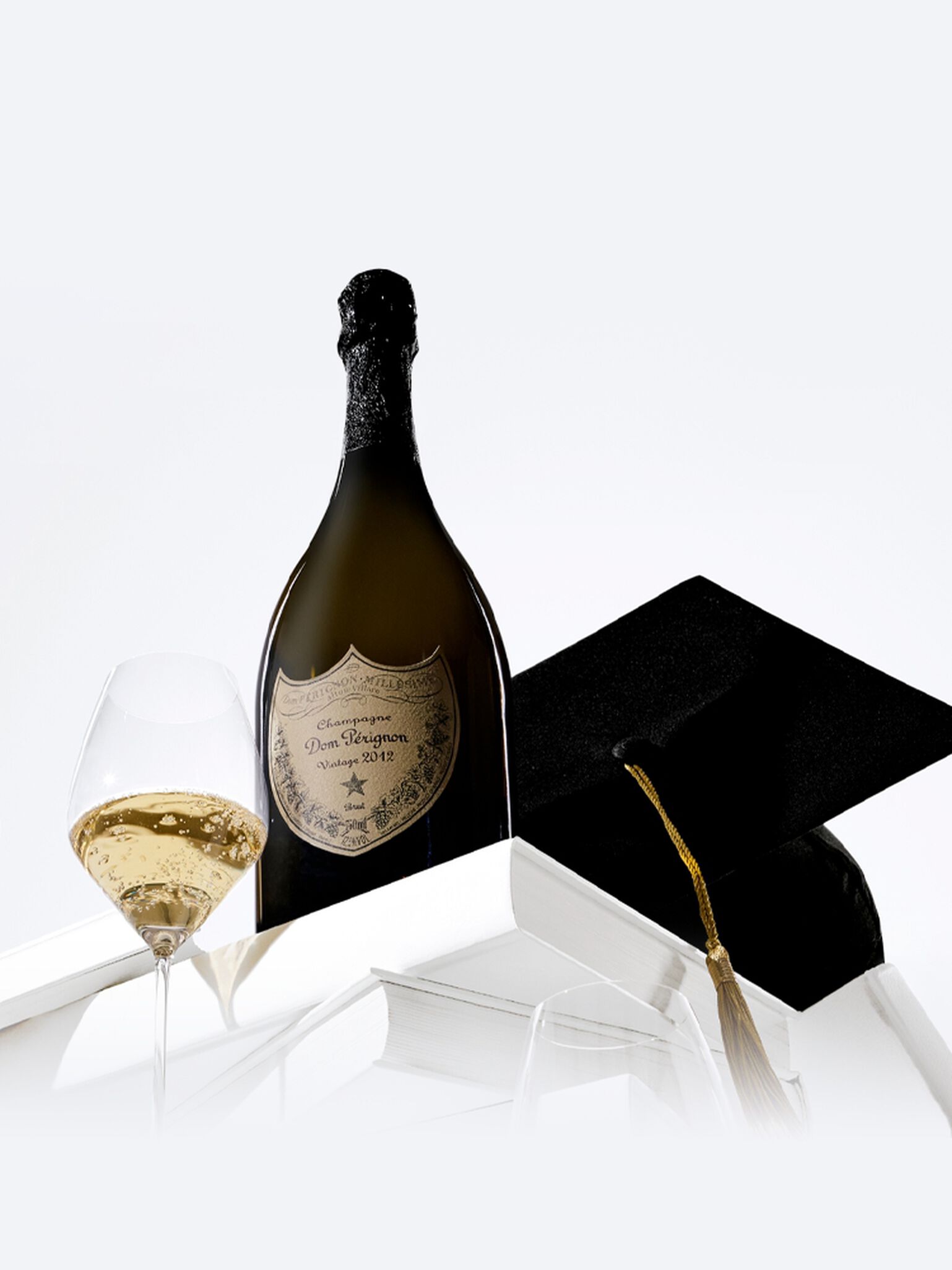 A bottle of Dom Perignon champagne with two flute glasses and a Graduation hat