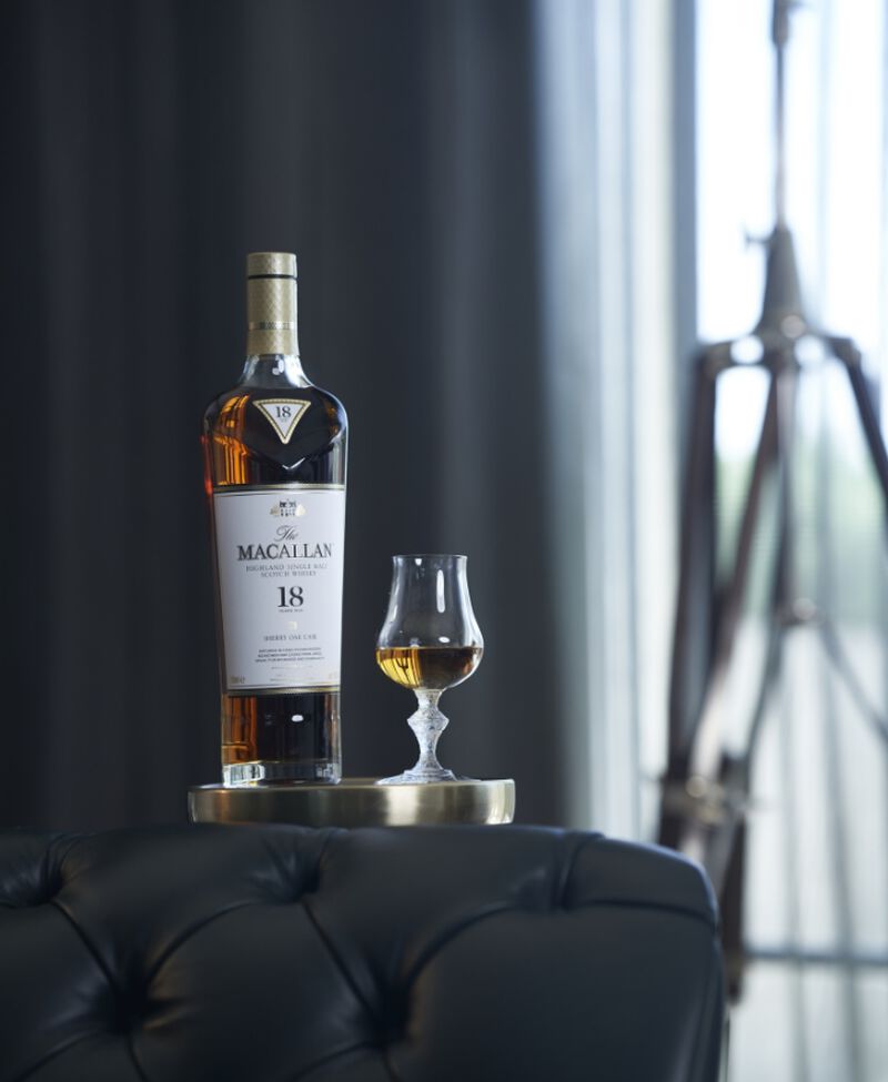Bottle of The Macallan Sherry Oak 18 Years Old sitting on a table with a glass, next to a couch