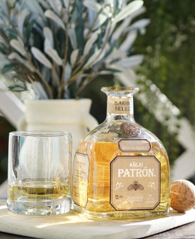 A bottle of Patron Single Barrel Anejo hand selected by our team, with a glass and greenery