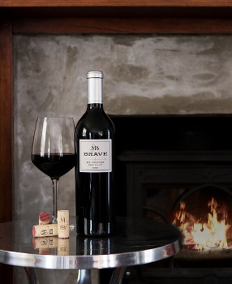 Bottle of Mt Brave Veeder Cabernet Sauvignon with a glass in front of a fireplace
