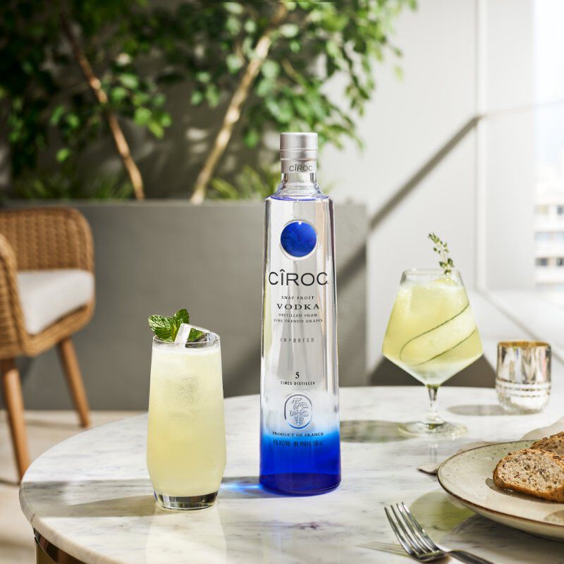 Bottle of Cîroc Vodka atop a marble table with two cocktails