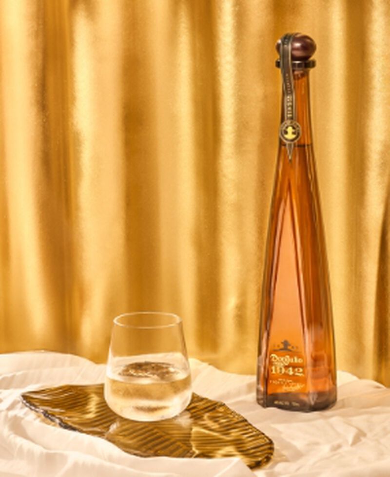 Bottle of Don Julio 1942 with glass in front of gold curtain