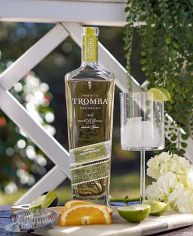 A bottle of Isle of Tequila Tromba Single Barrel Reposado S1B48 with a glass sitting outside with greenery in the background