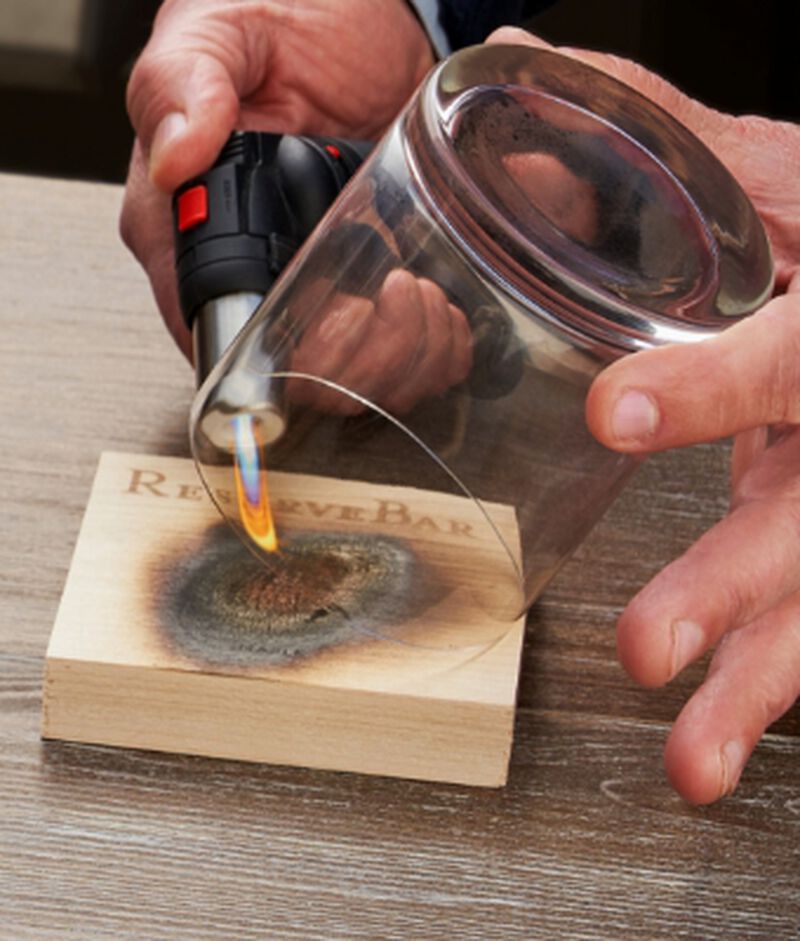 ReserveBar Smoking Kit being used to smoke a glass with a flame and wood plank