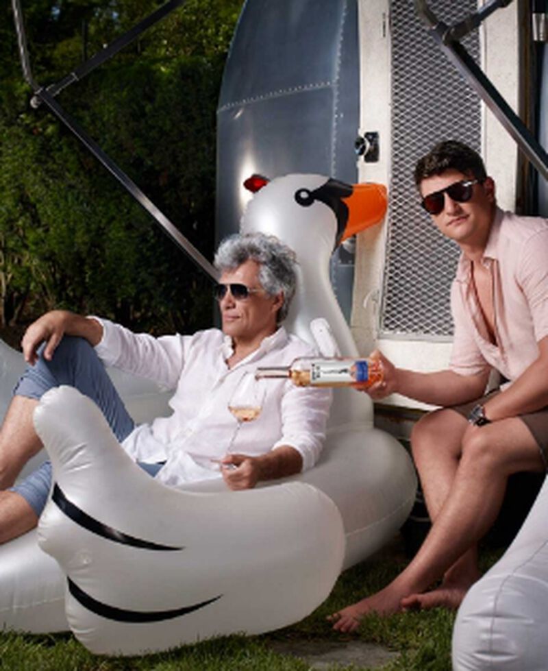 Bon Jovi sitting on a pool raft and enjoying a bottle of Hampton Water Rosé