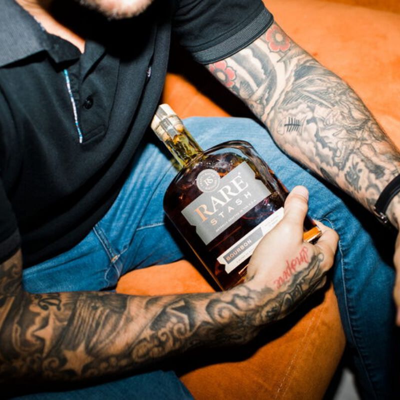 A bottle of Rare Stash being held by a man with tattoos