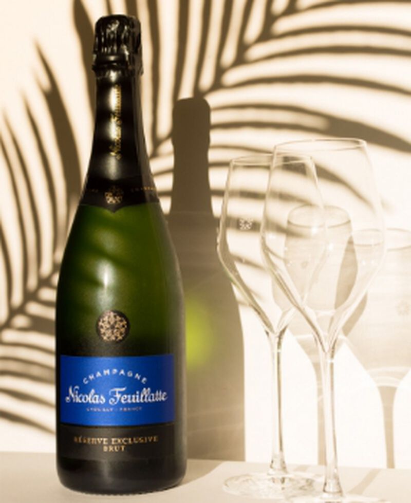 Bottle of Nicolas Feuillatte Réserve Exclusive Brut with two champagne flutes and a shadow from a palm tree
