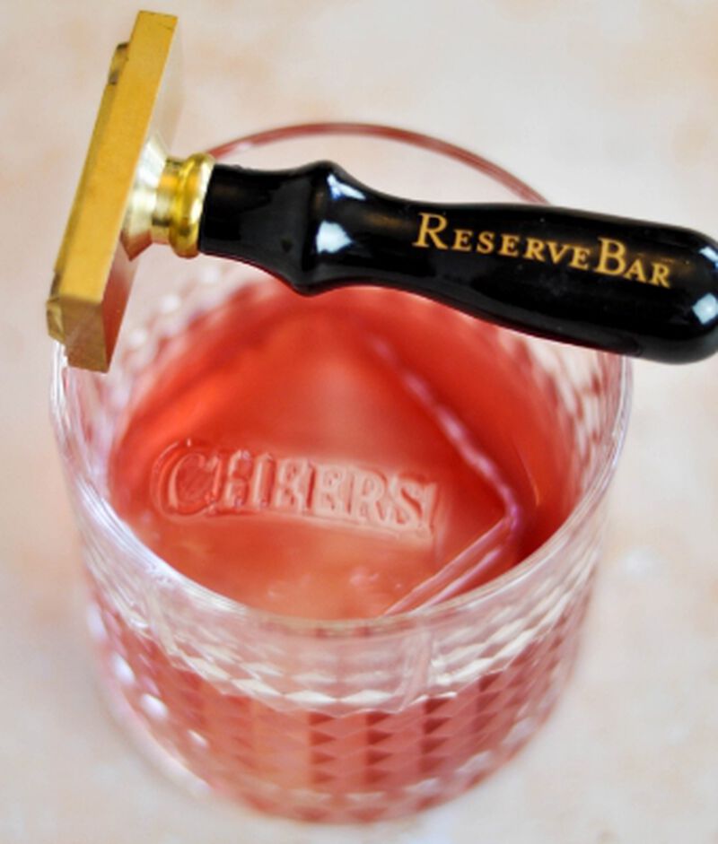 A cocktail with "Cheers" stamped into the ice cube using the ReserveBar Ice Stamp - "Cheers"