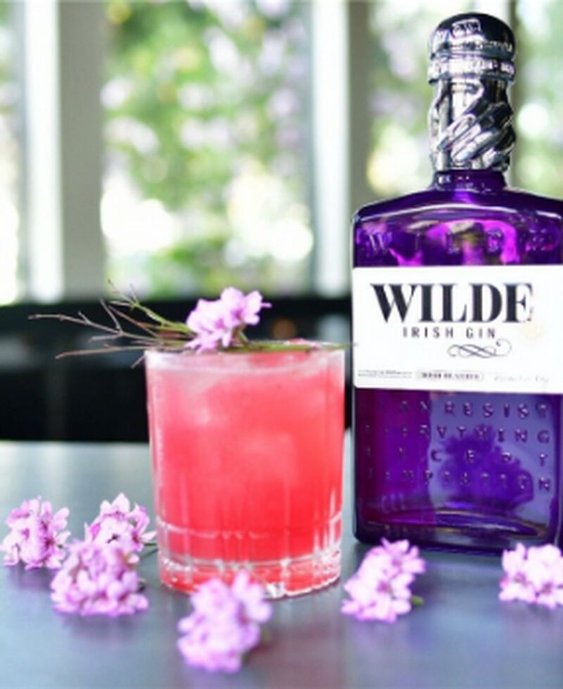 A bottle of Wilde Irish Gin with flowers and a cocktail